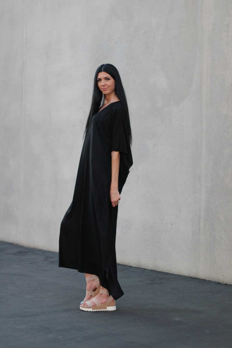 May include: A woman wearing a long black maxi dress with a v-neck and short sleeves. She is wearing nude platform sandals.