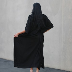 May include: A woman wearing a long black maxi dress with a long-sleeved, kimono-style top. She is wearing beige platform sandals.