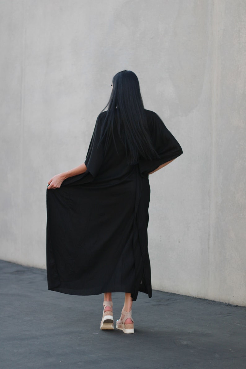 May include: A woman wearing a long black maxi dress with a long-sleeved, kimono-style top. She is wearing beige platform sandals.
