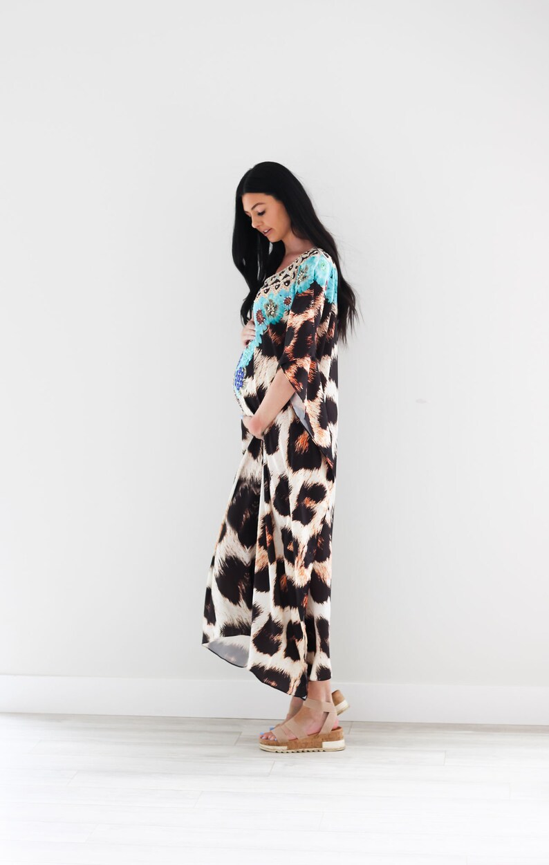 K&ouml;nnte beinhalten: Eine Frau tr&auml;gt ein langes, flie&szlig;endes Maxikleid mit Leopardenmuster. Das Kleid hat ein blaues und wei&szlig;es Blumenmuster auf der oberen H&auml;lfte. Sie steht vor einer wei&szlig;en Wand und tr&auml;gt braune Sandalen.