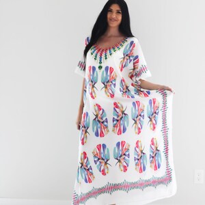 May include: White maxi dress with a colourful floral print and a beaded neckline. The dress has a flowing silhouette and a relaxed fit.