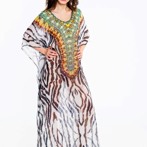 May include: A long, flowing kaftan dress with a zebra stripe pattern in black and white. The neckline and upper chest area feature a colorful, ornate design with shades of green, yellow, orange, and brown. The dress is paired with platform heels.