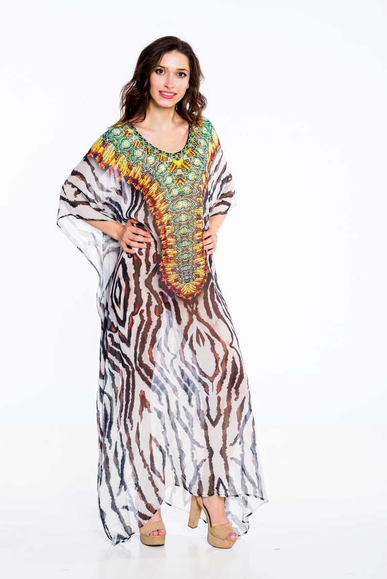 May include: A long, flowing kaftan dress with a zebra stripe pattern in black and white. The neckline and upper chest area feature a colorful, ornate design with shades of green, yellow, orange, and brown. The dress is paired with platform heels.