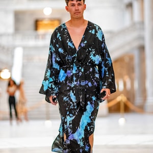 May include: A person wearing a long, black and blue tie-dye robe with a V-neck and a belt. The robe has a flowing, loose fit and is made of a soft, comfortable fabric.