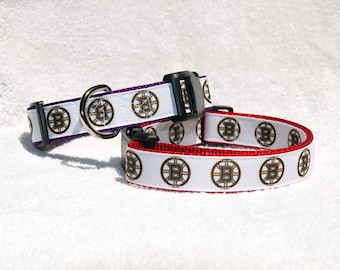 May include: Two dog collars with a white background and a repeated pattern of the Boston Bruins logo. One collar is purple and the other is red.