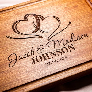May include: A wooden cutting board with two intertwined hearts engraved on the surface. The text "Jacob & Madison JOHNSON 02.14.2024" is also engraved on the board.