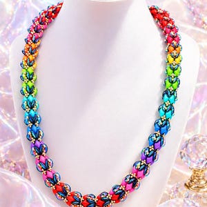 May include: A vibrant, handmade necklace displayed on a white bust. The necklace features a rainbow of colors, including red, pink, orange, yellow, green, blue, and purple. The beads are accented with gold-colored details, creating a striking piece of jewelry.