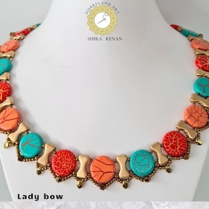 Può includere: Una collana colorata con perline turchesi, corallo e oro. La collana è realizzata con un motivo ripetitivo di tre perline, e le perline sono tutte rotonde e hanno una superficie testurizzata. La collana si chiama "Lady bow".