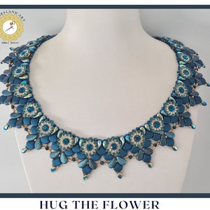 Può includere: Una collana di perline blu turchese e oro con un motivo floreale. La collana si chiama "Hug the Flower".