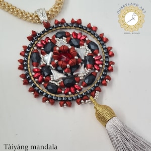 May include: A red, black and silver beaded necklace with a mandala pendant and a grey tassel. The pendant is a circle with a repeating pattern of beads. The necklace is called "Taiyang mandala".