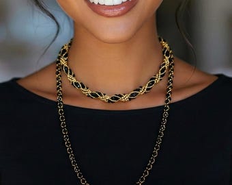 May include: A long necklace featuring a twisted design of small black beads and metallic gold beads. The necklace is layered, with a shorter, thicker twisted section resting near the neck and a longer, thinner strand hanging down in a loop.