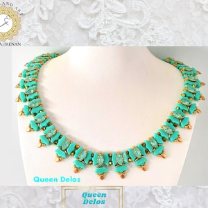 Può includere: Una collana di perline turchesi e dorate con un design delicato. La collana si chiama "Queen Delos" ed è esposta su uno sfondo bianco.