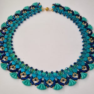 May include: A turquoise and navy blue beaded necklace with a fan-like design. The necklace features a variety of beads, including small gold-colored beads, and is secured with a gold-colored clasp. The necklace is a statement piece.