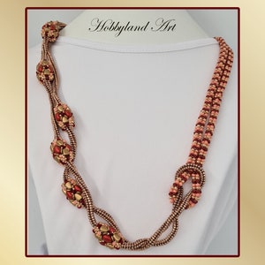 Op de afbeelding: Een lange, meerstrengs ketting met een geknoopt ontwerp. De ketting is gemaakt van kleine, gouden, rode en perzikkleurige kralen. De ketting wordt getoond op een wit manekin.