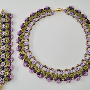May include: A set of purple, green and gold beaded jewellery, comprising a necklace and a bracelet. The necklace has a clasp fastening and the bracelet has a gold clasp.