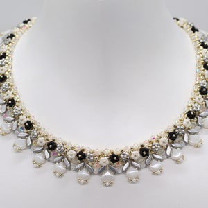 May include: A delicate silver, white, and black beaded necklace with a floral design. The necklace is made with small, round beads and features a cascading pattern.