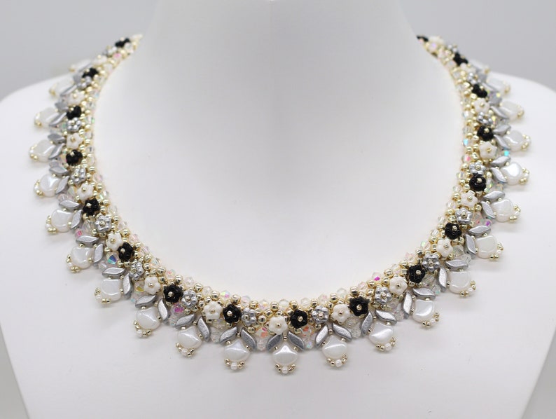 May include: A delicate silver, white, and black beaded necklace with a floral design. The necklace is made with small, round beads and features a cascading pattern.