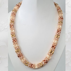 Peut inclure: Un collier de perles dorées, rose gold et crème. Le collier est composé de petites perles rondes et est enfilé sur une chaîne délicate.