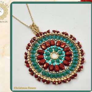 Pode incluir: Um colar de corrente de ouro com um pingente redondo que apresenta um design de mandala colorido. O pingente é feito de contas vermelhas, verdes e turquesa. O pingente é etiquetado como "Christmas flower".