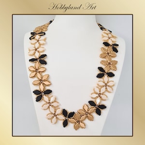 May include: A long necklace made of black, gold, and white beads. The beads are arranged in a flower pattern.