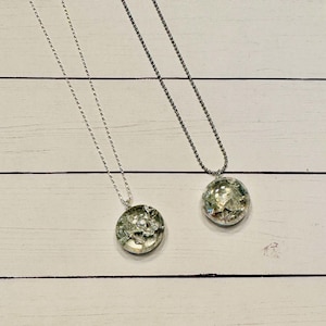May include: Two silver necklaces with round glass pendants. The pendants are filled with iridescent pieces of glass.