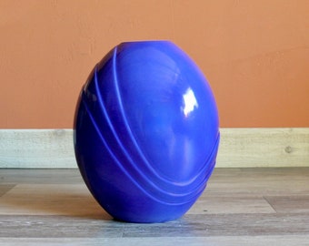 May include: A blue ceramic vase with a smooth, glossy finish and a unique, curved design. The vase has a rounded shape and is perfect for displaying flowers or other decorative items.