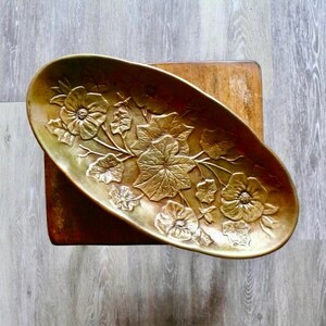 May include: An oval-shaped brass serving dish with a floral design. The dish is embossed with leaves and flowers.