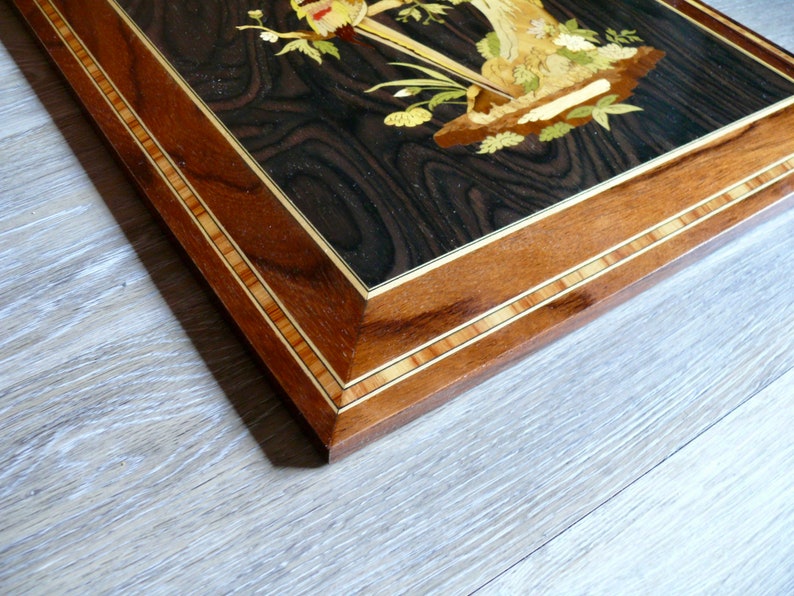 K&ouml;nnte beinhalten: Ein Holzrahmen mit einem detaillierten Intarsiendesign. Der Rahmen ist aus dunklem Holz mit einer Einlage aus hellem Holz. Der Rahmen hat eine rechteckige Form.