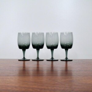 May include: A set of four matching wine glasses featuring a distinct ombre effect, transitioning from a deep, dark charcoal gray at the base of the bowl and stem to a lighter, translucent gray at the rim, standing on circular glass bases.