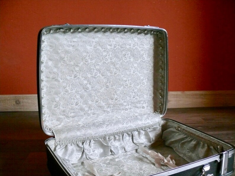 May include: A vintage silver suitcase with a white floral lining. The suitcase is open and the lining is visible.