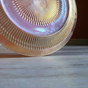 Puede incluir: Un plato de vidrio iridiscente vintage con un patr&oacute;n de diamante. El plato es de color rosa claro con un brillo dorado.
