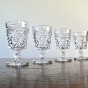 May include: Four clear glass goblets with a cut glass design. The goblets are arranged in a row from largest to smallest.