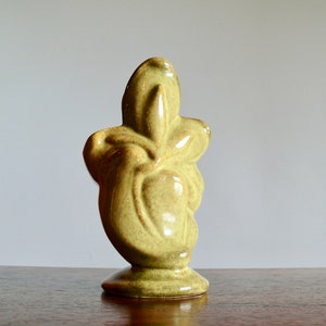 K&ouml;nnte beinhalten: Eine hellgr&uuml;ne Keramikskulptur mit Sockel. Die abstrakte Form hat eine glatte, gl&auml;nzende Oberfl&auml;che und eine einzigartige, organische Form. Die Skulptur wird auf einer Holzoberfl&auml;che vor einem neutralen Hintergrund ausgestellt.