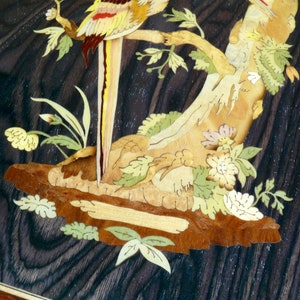 K&ouml;nnte beinhalten: Intricate Holzmarqueterie-Kunstwerk mit einem gelben und roten Vogel, der auf einem Ast mit gr&uuml;nen Bl&auml;ttern und Blumen sitzt. Der Hintergrund ist eine dunkle Holzmaserung.