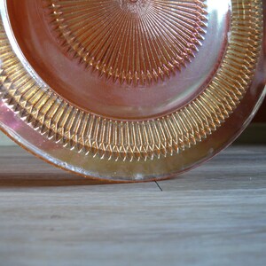 Puede incluir: Un plato de vidrio rosa iridiscente vintage con un borde festoneado y un dise&ntilde;o de sol en el centro.