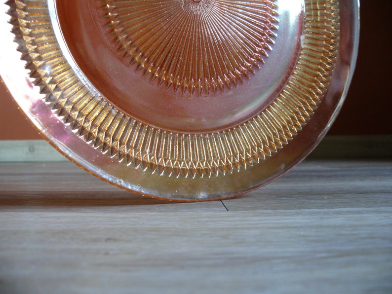 Puede incluir: Un plato de vidrio rosa iridiscente vintage con un borde festoneado y un dise&ntilde;o de sol en el centro.