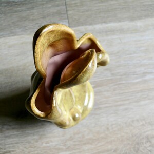 K&ouml;nnte beinhalten: Eine einzigartige Keramikvase mit einer wellenf&ouml;rmigen, organischen Form. Die Au&szlig;enseite ist ein ged&auml;mpftes, gelblich-gr&uuml;n, w&auml;hrend die Innenseite eine weiche, staubige Rosafarbe hat. Die Vase hat eine gl&auml;nzende Oberfl&auml;che und scheint handgefertigt zu sein.