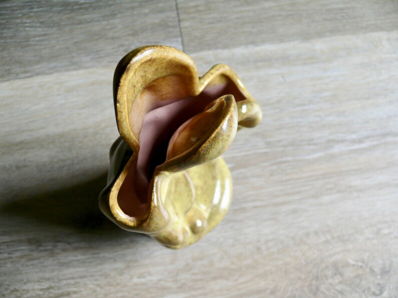 K&ouml;nnte beinhalten: Eine einzigartige Keramikvase mit einer wellenf&ouml;rmigen, organischen Form. Die Au&szlig;enseite ist ein ged&auml;mpftes, gelblich-gr&uuml;n, w&auml;hrend die Innenseite eine weiche, staubige Rosafarbe hat. Die Vase hat eine gl&auml;nzende Oberfl&auml;che und scheint handgefertigt zu sein.