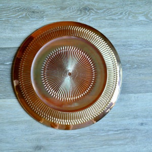 Puede incluir: Un plato de servicio dorado con un dise&ntilde;o decorativo en forma de sol. El plato tiene un borde elevado y una superficie lisa y brillante.