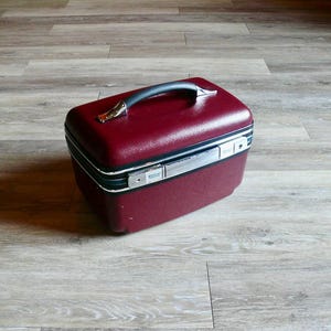 May include: A burgundy hard-sided travel case with a silver handle and trim.