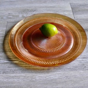 Puede incluir: Una bandeja redonda de servir de vidrio &aacute;mbar con un patr&oacute;n decorativo en forma de diamante. Un solo lim&oacute;n verde se encuentra en el centro de la bandeja.