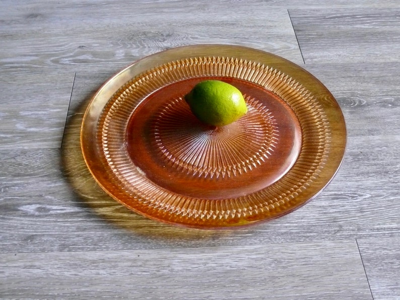 Puede incluir: Una bandeja redonda de servir de vidrio &aacute;mbar con un patr&oacute;n decorativo en forma de diamante. Un solo lim&oacute;n verde se encuentra en el centro de la bandeja.