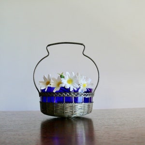 May include: A silver wire basket with a blue glass liner and white flowers.