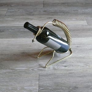 May include: A gold metal wine bottle holder with a spring-shaped design. The holder is holding a bottle of wine.