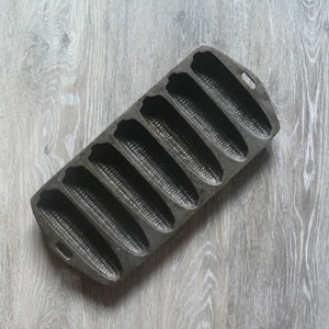 May include: A vintage cast iron cornbread pan with eight individual molds. The pan is gray and has a rustic look.