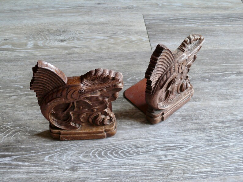 May include: A pair of wooden bookends shaped like fish. The bookends are carved with intricate details and have a dark brown finish.