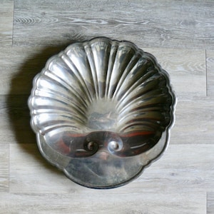 May include: A silver serving dish shaped like a seashell with a fluted design.
