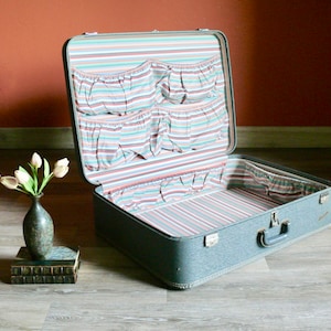 May include: A vintage gray suitcase with a striped fabric lining and multiple pockets. The suitcase is open and empty.