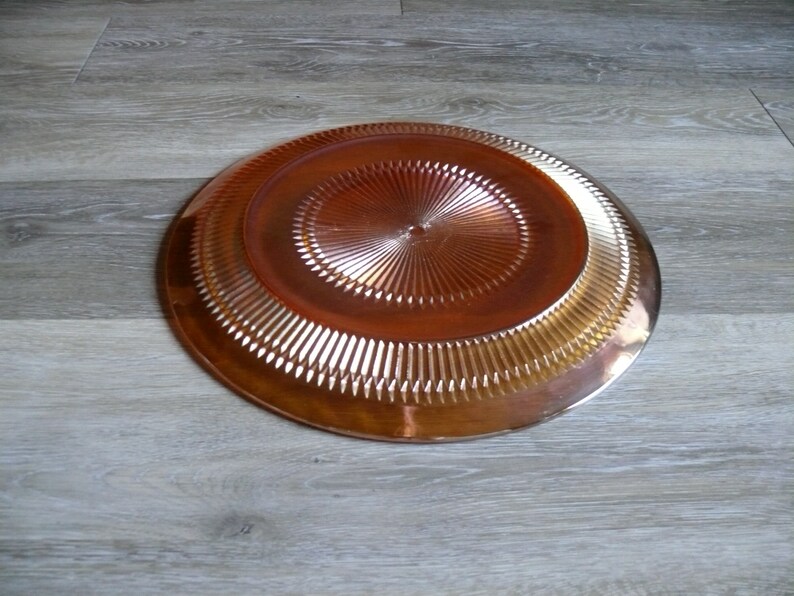 Puede incluir: Un plato grande, redondo, de vidrio &aacute;mbar con un patr&oacute;n decorativo en forma de diamante. El plato tiene una superficie brillante y reflectante.