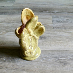 K&ouml;nnte beinhalten: Eine Vintage-Keramikvase in Form einer stilisierten Blume, mit hellgr&uuml;ner Au&szlig;enseite und rosa Innenraum. Die Vase hat eine strukturierte Oberfl&auml;che und einen abgerundeten Boden. Die bl&uuml;tenartige &Ouml;ffnung ist breit und offen.